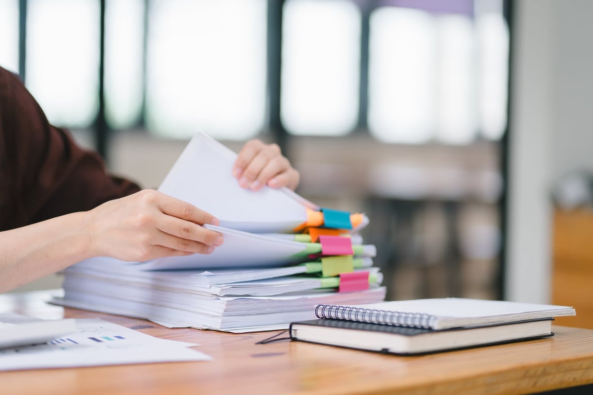 Hands sorting through stacks of paper case files on a desk