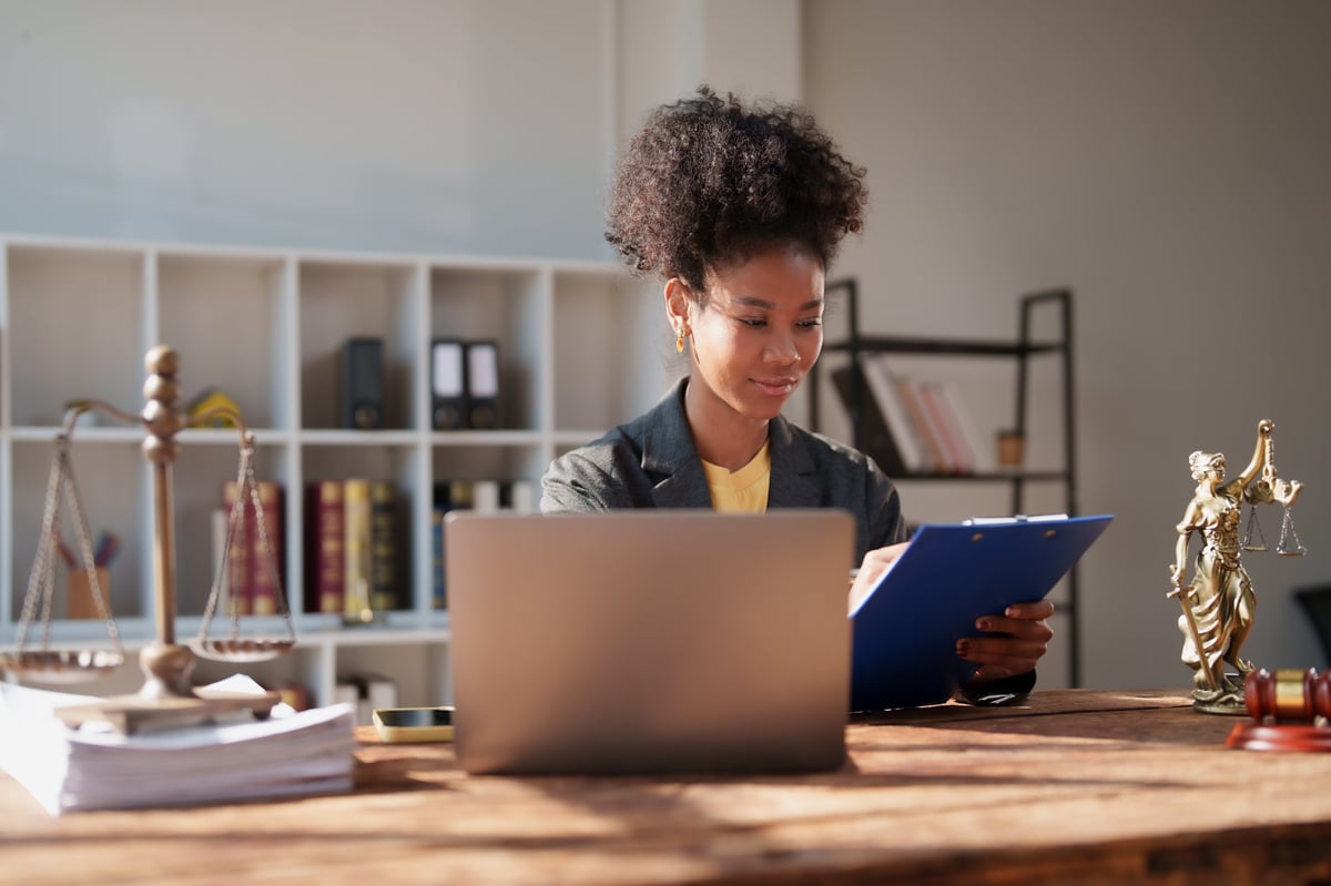 Paralegal reviewing legal documents at a desk with a laptop and scales of justice
